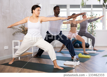 Young woman with group of active people exercising full body stretching workout during yoga classes in gym 133462333