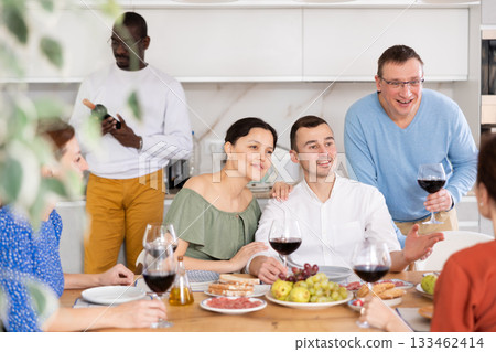 Middle-aged friends sitting at table with a glass of wine while having friendly conversation Middle-aged friends sitting at table with a glass of wine while having friendly conversation 133462414