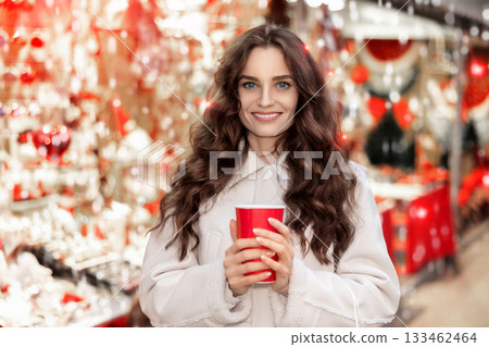 Cheerful woman with paper cup of hot tea walking at Christmas street fair 133462464