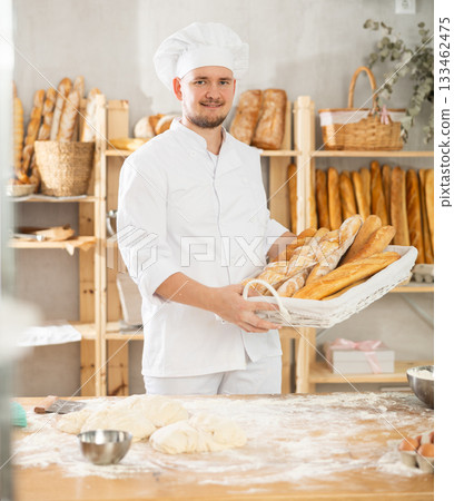 Male baker holds basket with finished products, shows many different baguettes Male baker holds basket with finished products, shows many different baguettes 133462475