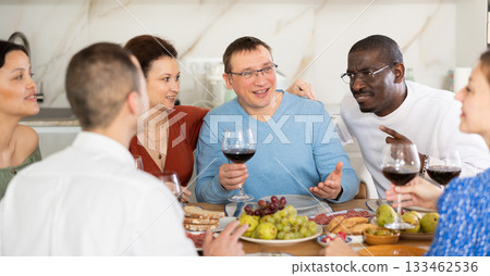 Middle-aged friends sitting at table with a glass of wine while having friendly conversation 133462536