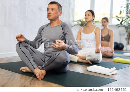 Positive man in sports clothes having yoga class in group sitting in lotus pose in yoga studio 133462561