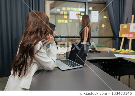 Conference room hosts business women team meeting, people collaborating on project, woman presenting innovative ideas on clear wall, laptop ready fostering productive work environment. Conference room hosts business women team meeting, people collaborating on project, woman presenting innovative ideas on clear wall, laptop ready fostering productive work environment. 133463140