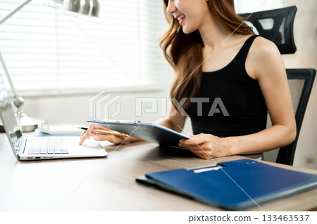 Confident Asian woman with a smile standing holding notepad and tablet at the modern office. Confident Asian woman with a smile standing holding notepad and tablet at the modern office. 133463537