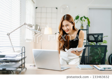 Smiling Asian woman standing in bright modern home office using smartphone, concept of digital lifestyle, communication, and remote working success. 133463632