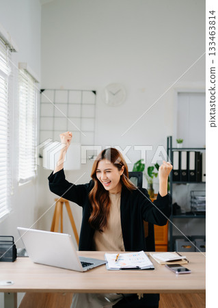 Asian businesswoman celebrating success in modern office, holding tablet and smiling with laptop, showing joy and achievement in work, startup, and digital business. Asian businesswoman celebrating success in modern office, holding tablet and smiling with laptop, showing joy and achievement in work, startup, and digital business. 133463814