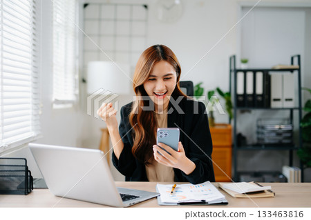 Asian businesswoman celebrating success in modern office, holding tablet and smiling with laptop, showing joy and achievement in work, startup, and digital business. Asian businesswoman celebrating success in modern office, holding tablet and smiling with laptop, showing joy and achievement in work, startup, and digital business. 133463816