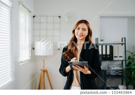 Confident Asian businesswoman smiling and giving thumbs up while holding tablet in modern office Confident Asian businesswoman smiling and giving thumbs up while holding tablet in modern office 133463864
