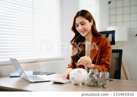 Smiling businesswoman saves money with piggy bank and coins. Ideal for finance, savings, budgeting, and office 133463930