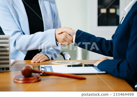 Business handshake in office with lawyer, cash, gavel, and building model. Concept of real estate deal, legal agreement, property contract, and investment success. 133464499