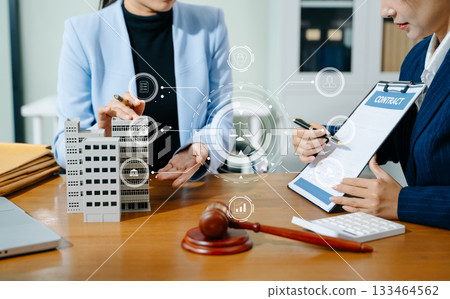 Female lawyer and client discuss legal contract with digital finance icons. Modern law, real estate, tech innovation, and business consulting in one powerful scene. 133464562