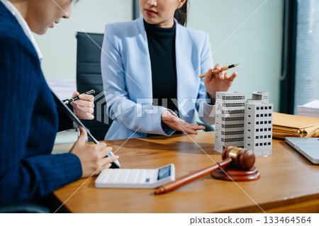 Two professional women reviewing a real estate contract with gavel, building model, and paperwork. Business law, legal advice 133464564