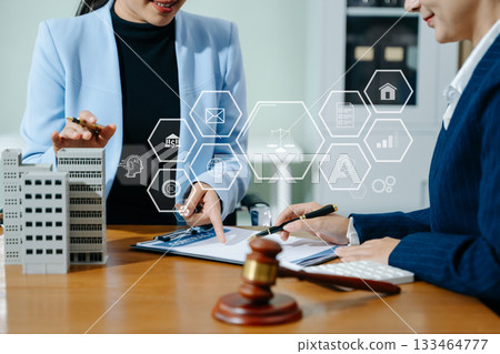Female lawyer and client discuss legal contract with digital finance icons. Modern law, real estate, tech innovation, and business consulting in one powerful scene. 133464777