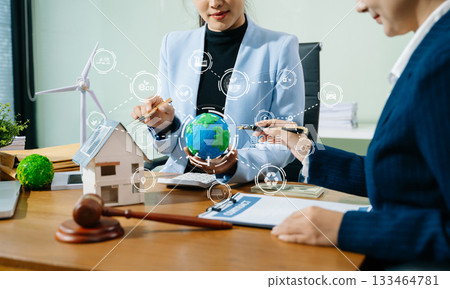 Two businesswomen plan sustainable energy strategies with global models, legal contracts, and smart eco tech to drive green innovation 133464781