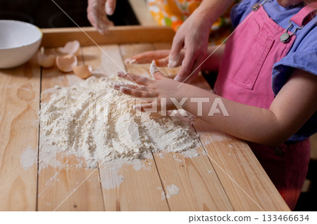 Child and adult engaging in flour preparation, Little hands learning to knead dough with guidance, Young child and adult sharing playful baking experience in warm kitchen Child and adult engaging in flour preparation, Little hands learning to knead dough with guidance, Young child and adult sharing playful baking experience in warm kitchen 133466634