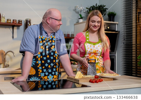 Caucasian pair grating cheese over dish metal grater in hand, bowl below, grated shavings, bright countertop, partner watching and laughing, ingredientfocused scene Caucasian pair grating cheese over dish metal grater in hand, bowl below, grated shavings, bright countertop, partner watching and laughing, ingredientfocused scene 133466638