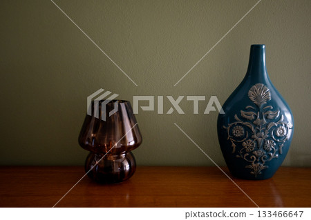 Stylish vintage setup with contrasting materials highlighting elegance, Decorative arrangement featuring colorful ceramics and translucent glassware with warm lighting 133466647