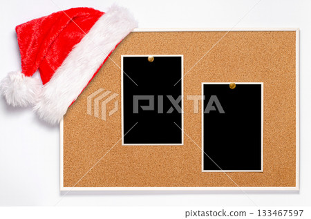 Blank photos are pinned to the board. Santa's hat on a cork board. 133467597