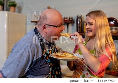 Joyful father and daughter meal, Laughter as family bonds over supper, Happy family sharing pizza in cozy kitchen surrounded by colorful decorations and retro appliances 133467708