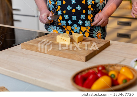 Homely cooking setup, Casual kitchen moment with food and sunlight, Comfortable kitchen environment showing home cook slicing cheese amid colorful fresh produce Homely cooking setup, Casual kitchen moment with food and sunlight, Comfortable kitchen environment showing home cook slicing cheese amid colorful fresh produce 133467720