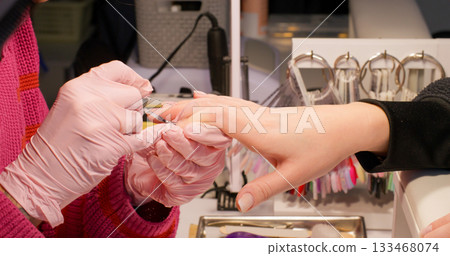 Gel nails. Professional manicure procedure. Female hand in gloves getting cover treatment with acrylic nude polish by beauty technician in salon. Gel nails. Professional manicure procedure. Female hand in gloves getting cover treatment with acrylic nude polish by beauty technician in salon. 133468074