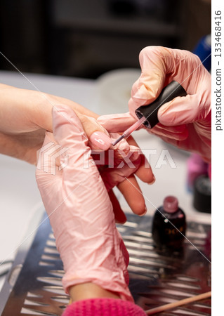 Professional hand care. Hardware manicure. Female cosmetology master coating nails with pastel gel polish in beauty salon procedure. 133468416