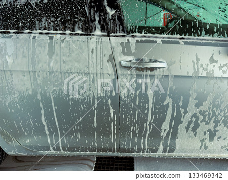 Shimmering bubbles coat a silver car as it goes through a vibrant automatic car wash on a sunny afternoon 133469342