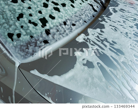 Shimmering suds blanket a silver car during a sunny afternoon wash in a lively neighborhood garage Shimmering suds blanket a silver car during a sunny afternoon wash in a lively neighborhood garage 133469344