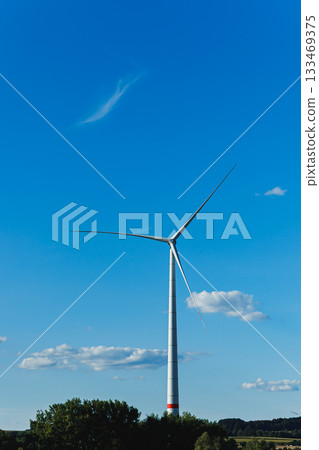 Wind turbine stands tall against a clear blue sky with scattered clouds, showcasing renewable energy's promise in a serene landscape 133469375