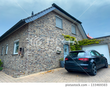 Charming brick house with a modern car parked outside in a quaint neighborhood during overcast weather 133469383