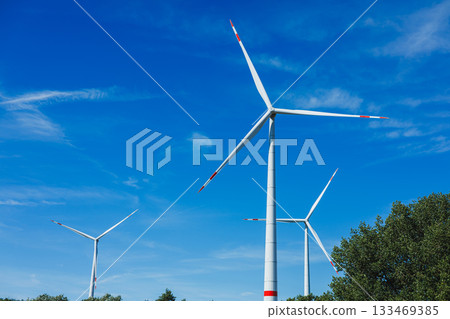 Capturing three large wind turbines against a bright blue sky in a rural landscape during the daytime 133469385
