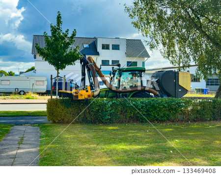 Busy morning with a large green machine cleaning up the street in a quiet neighborhood under a partly cloudy sky 133469408