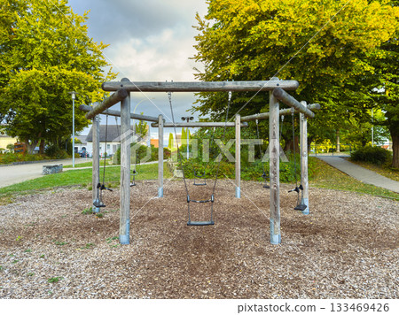 Swings under a cloudy sky in a tranquil playground set amidst blossoming trees on a quiet autumn afternoon 133469426