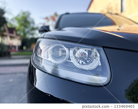 Close-up view of a stylish car headlight in a sunlit neighborhood, showcasing sleek design and modern technology during a tranquil autumn afternoon 133469465