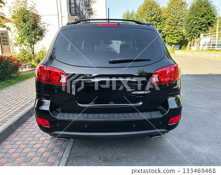 Black SUV parked on a sunny street lined with trees and flowers, showcasing its sleek design and polished exterior during a clear afternoon Black SUV parked on a sunny street lined with trees and flowers, showcasing its sleek design and polished exterior during a clear afternoon 133469468