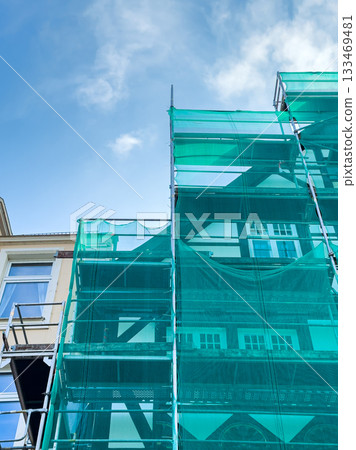 Renovation project underway with bright blue sky and green scaffolding covering a historic building facade Renovation project underway with bright blue sky and green scaffolding covering a historic building facade 133469481