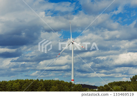 Majestic wind turbine stands tall against a dramatic sky filled with fluffy clouds and vibrant greens of nature in a serene landscape at midday 133469519