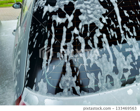 Soapy bubbles cascading down a car window during a bright afternoon car wash at a local service station in the city 133469563