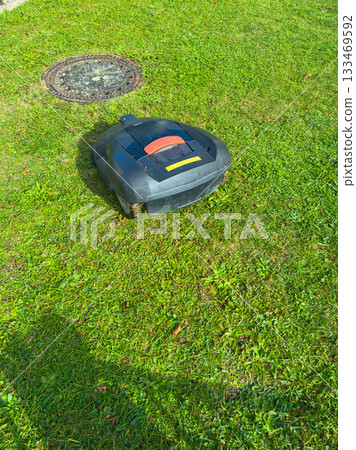 Robot mower navigating a green lawn under bright sunlight during a serene afternoon in a suburban neighborhood 133469592