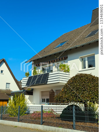 Modern home in a sunny neighborhood showcases solar panels and vibrant greenery on a clear blue sky day 133469601