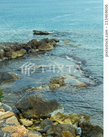 Relaxing coastal scene where calm waters meet rugged rocks under a serene sky at midday on a tranquil beach Relaxing coastal scene where calm waters meet rugged rocks under a serene sky at midday on a tranquil beach 133469606