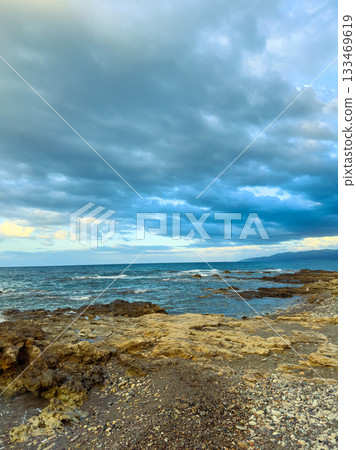 Waves crash against rocky shore under a cloudy sky during twilight on a peaceful evening by the coast 133469619