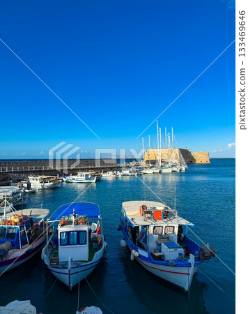 Colorful boats moored in a serene harbor under a bright blue sky near a historic fortress at midday Colorful boats moored in a serene harbor under a bright blue sky near a historic fortress at midday 133469646