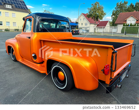 Classic orange truck shines under the bright sky in a vibrant neighborhood, showcasing vintage style and custom modifications in broad daylight 133469652
