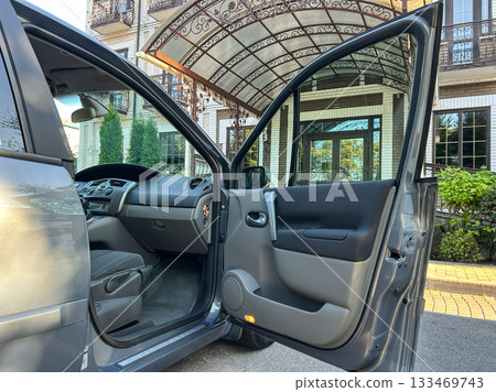 Experience the open door of a silver car parked outside a charming building with elegant architecture on a sunny day Experience the open door of a silver car parked outside a charming building with elegant architecture on a sunny day 133469743