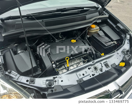 Engine bay exposed with intricate machinery showcasing mechanical precision in a modern car at a busy garage during the day Engine bay exposed with intricate machinery showcasing mechanical precision in a modern car at a busy garage during the day 133469775