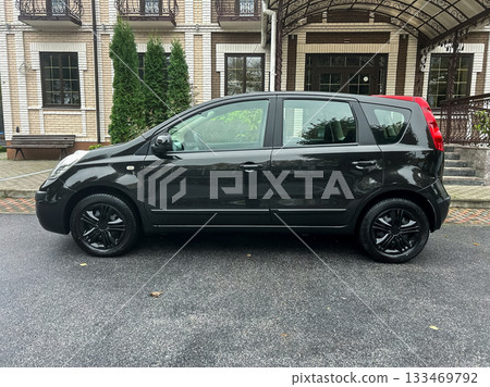 Compact black car parked under a canopy outside a stylish building surrounded by greenery on a rainy day Compact black car parked under a canopy outside a stylish building surrounded by greenery on a rainy day 133469792
