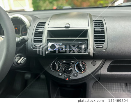 Dashboard of a compact car featuring a radio and climate controls, with afternoon sunlight illuminating the interior Dashboard of a compact car featuring a radio and climate controls, with afternoon sunlight illuminating the interior 133469804