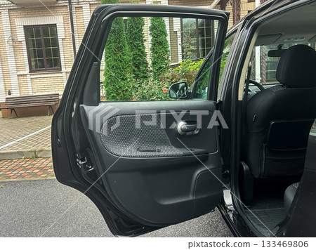 Car door swings open to reveal a quiet outdoor space with lush greenery and brick pathways, inviting exploration on a serene day 133469806