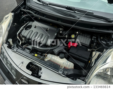 Engine components displayed in a compact vehicle's open hood revealing intricate machinery and parts in a car maintenance setting 133469814
